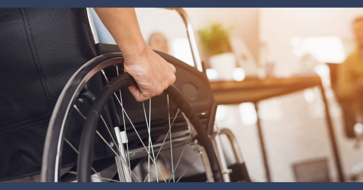 Close up image of a man in a wheelchair rolling towards an office desk