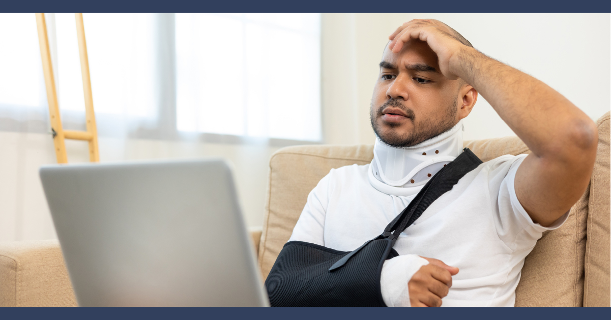 Man wearing a medical shoulder sling looking at his laptop computer with distress